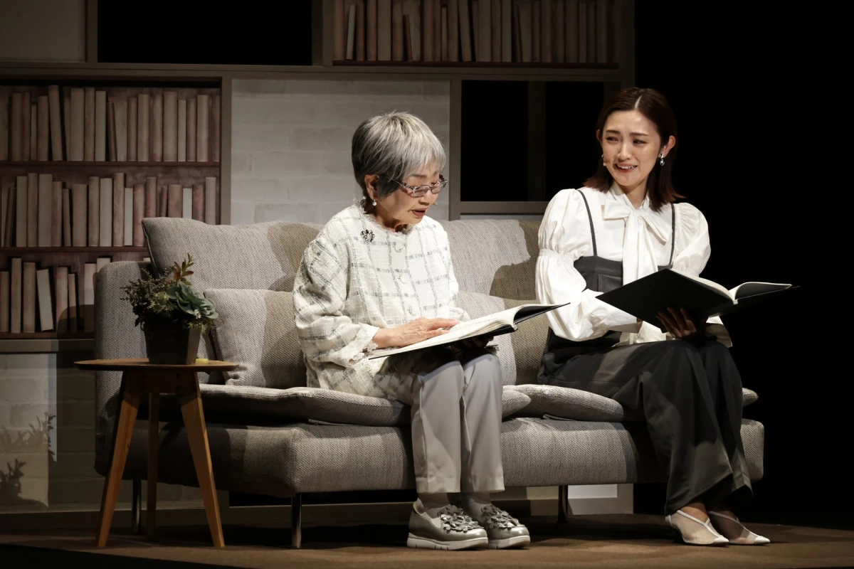 本棚のある室内で、二人の女性がソファに座り、それぞれ本を読んでいます