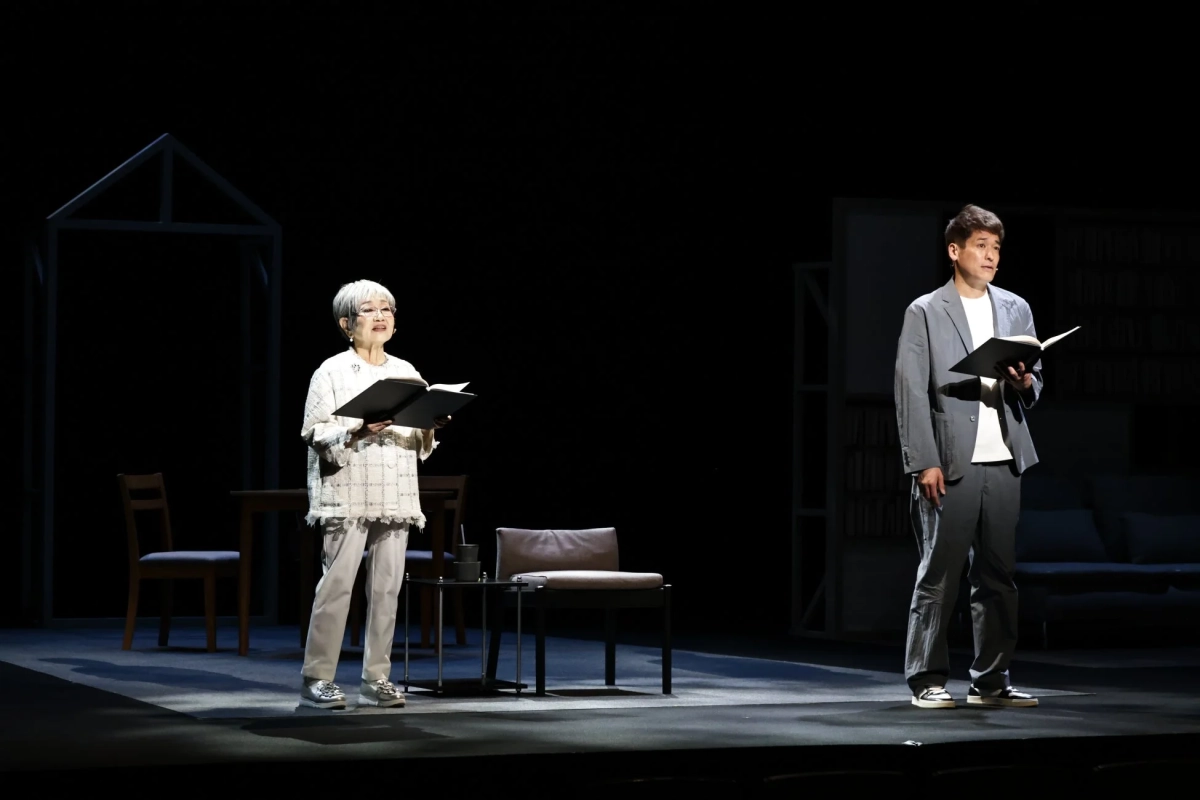 舞台上で、本を手に持つ男女二人がスポットライトを浴びて立っている