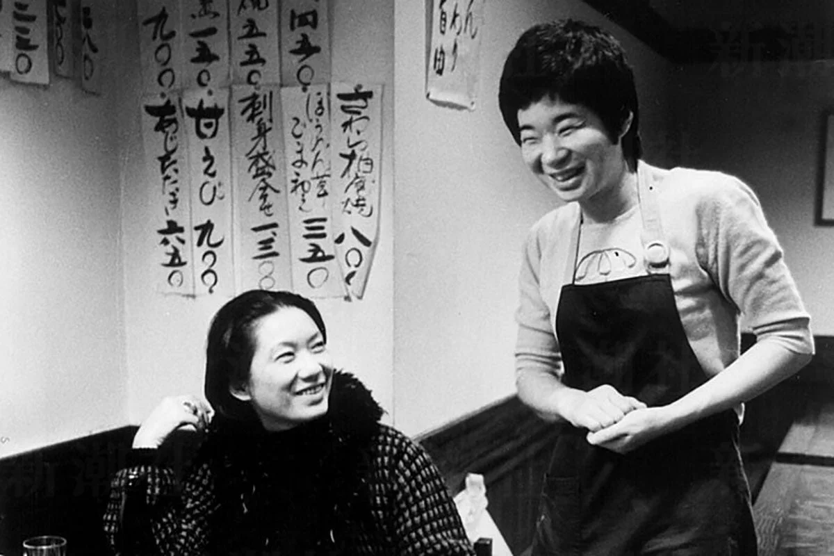 カジュアルな飲食店で笑顔を交わす二人の日本人女性が写る白黒写真。